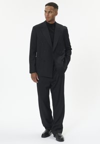 Juodas dvigubos sagtys švarkas su dviem priekinėmis kišenėmis, derinamas su laisvai krintančiomis juodomis kelnėmis ir juodais batais. Paprastas, oficialus dizainas.