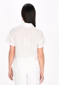 Camicia corta a maniche corte bianca in tessuto a rete con motivi a pois, colletto e vestibilità rilassata, vista da dietro.