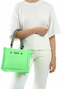 Neon groene tote tas met een gewatteerd ontwerp, zwarte en groene gevlochten handvatten, zilveren hardwareaccenten en contrasterende zwarte stikseldetails.