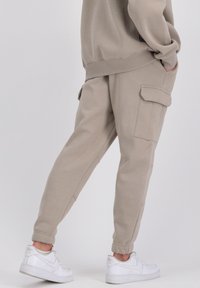Béžové cargo nohavice vyrobené z jemného materiálu, s dvoma bočnými vreckami, zúženými manžetami a voľným strihom, skombinované s bielymi teniskami.
