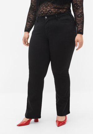 Sorte tætsiddende jeans med en glat overflade, fem-lomme design og metalknaplukning, parret med røde spidse hæle.