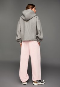 Sivá oversized mikina s kapucňou, skombinovaná s voľne strihanými ružovými teplákmi. Biele a sivé tenisky s priedušným sieťkovým dizajnom dopĺňajú súpravu.