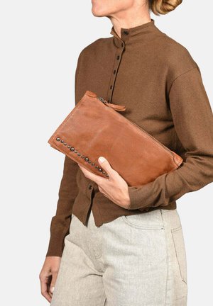 Bolso de mano de cuero marrón con cierre de cremallera, detalles de tachuelas laterales y una textura suave, sostenido por una persona que lleva una camisa marrón.