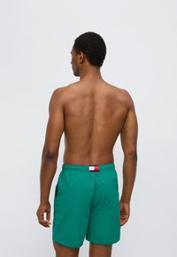 Πράσινα μαγιό βερμούδα κατασκευασμένα από ελαφρύ υλικό, με ελαστική μέση που έχει ρίγα σε κόκκινο, λευκό και μπλε. Διαθέτει τσέπες.