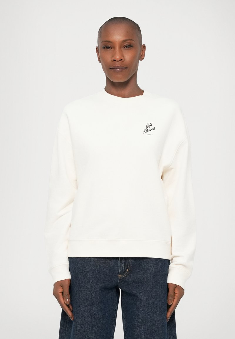 Felpa oversize colore crema con scollatura rotonda e polsini a costine, con un piccolo logo nero sul petto.