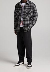 Svart och vit rutig skjortjacka med två bröstfickor över en grå tryckt t-shirt, i kombination med lösa svarta byxor och svarta sneakers.