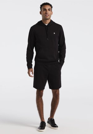 Sweat à capuche noir avec une poche avant et un cordon de serrage, associé à un short noir et des baskets noires. Texture lisse, design décontracté.