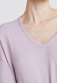 Maglione oversized viola chiaro con scollo a V, texture morbida e dettagli a coste lungo il colletto e le maniche.