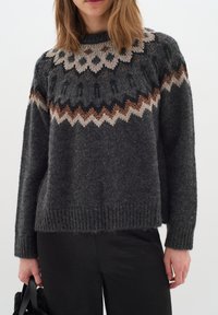 Pulover tricotat de culoare gri închis, cu un finisaj texturat, având un model geometric în nuanțe de crem și rugină pe guler și umeri.