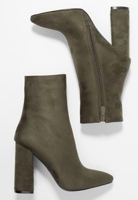 Bottines en suède vert olive, avec un bout pointu et un talon épais. Elles sont dotées d'une fermeture éclair sur le côté et d'une surface texturée pour un détail supplémentaire.