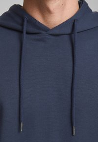 Hoodie en coton bleu marine avec cordons de serrage et embouts en métal, offrant une texture douce et un design décontracté.
