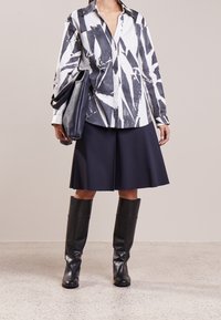 Vit skjorta med svart abstrakt tryck, matchad med en marinblå A-linje kjol och knähöga svarta läderstövlar; inkluderar en svart läderväska.