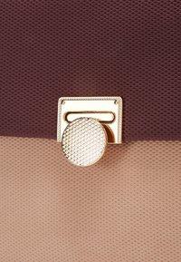 Gros plan sur une fermeture dorée texturée sur un sac à main avec des panneaux en tissu marron foncé en haut et beige clair en bas.