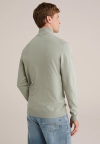 Gai zaļš, viegls pusvārds ar augstu apkakli, ribotām piedurknēm un apakšmalu; mīksta tekstūra; pieguļošs piegriezums; valkāts ar ziliem džinsiem.