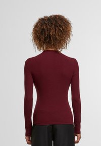 Burgundi színű, hosszú ujjú, testhezálló felső pamutanyagból, magas nyakkivágással és sima textúrával, testhez simuló kialakítással.