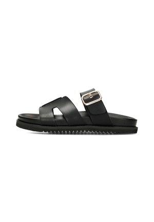 Schwarze Slide-Sandale mit zwei breiten Riemen, einer mit goldener Schnalle, und einer profilierten Laufsohle für besseren Grip.