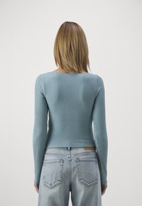 Blå ribbad långärmad topp med fyrkantig halsringning, bärs med ljusblå denimjeans som har standard bakfickor och en figursydd silhuett.