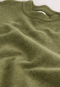 Oļīvzaļš adīts džemperis ar ribotu kakla izgriezumu, kas izceļ mīkstu, teksturētu audumu, kas gludi krīt. Dizains ir ikdienišķs un atslābināts.