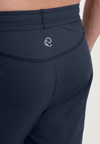 Marineblauwe sportleggings met een gladde textuur, voorzien van een zachte tailleband en een klein wit logo op de achterkant.