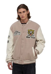Beżowa kurtka sportowa z kremowymi rękawami, z naszywką tigerską, haftem "Los Angeles" oraz paskowanym ściągaczem u dołu i przy mankietach.
