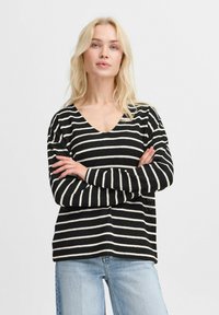 Gestreifter Pullover in Schwarz und Weiß mit V-Ausschnitt, langen �Ärmeln und einem lockeren Schnitt. Die Textur wirkt weich und gestrickt.