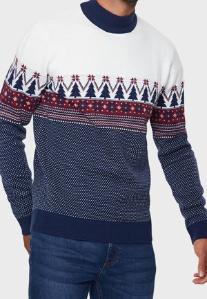 Strickpullover mit einem weißen oberen Teil und navy- und roten gemusterten Abschnitten, einschließlich Bäume und geometrische Designs, mit einem navy-ribbed Kragen.