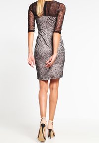 Grå åtsittande klänning med svarta spetsärm och texturerade blommönster. Klänningen har en bakficka och är matchad med nakna högklackade skor.