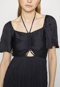 Μαύρο φόρεμα με κοντά αγκαθωτά μανίκια και τετράγωνη λαιμόκοψη. Διαθέτει συγκεντρωμένες λεπτομέρειες στο μπούστο και μικρή περικοπή με κορδόνια στο κέντρο.