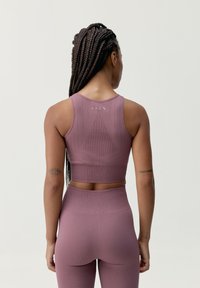 Sportinis kūno įformintas tankinis ir aukštai įsiūtos leginsai purpurinės spalvos su tekstūruotu raštu ir sustiprintomis siūlėmis. Pavyzdžiui, logotipas ant nugaros.