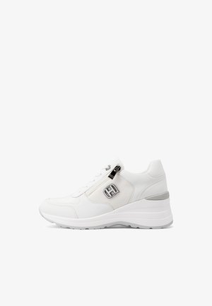 Sneaker bianca con suola a zeppa, cerniera laterale e un emblema con logo metallico su pannello di tessuto decorato.