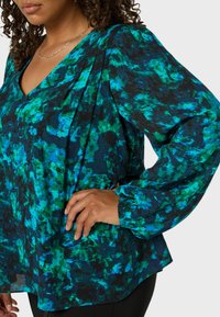 Färgglad blus med v-ringning, lång puffärmar och ett grönt och blått abstrakt mönster på svart bakgrund.