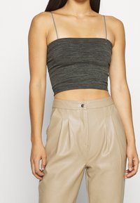 Top corto grigio a coste con spalline sottili; abbinato a pantaloni beige in pelle a vita alta con pieghe e chiusura frontale con bottoni.