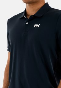 Camiseta polo navy de tela texturizada, con mangas cortas, una tapeta de tres botones y un logo blanco en el pecho.