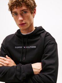 Felpa nera in cotone con testo bianco "TOMMY HILFIGER". Dotata di cordini regolabili, polsini a coste e vestibilità comoda.