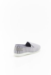Scarpa slip-on grigia con strisce verticali bianche, tomaia in tessuto, pannelli elastici laterali e un sottile accento grigio sul tallone. Suola in gomma bianca.