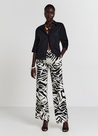 Camicia nera con bottoni e un design testurizzato, abbinata a pantaloni larghi a vita alta con una stampa zebra bianca e nera. Tacchi aperti neri.