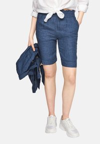 Pantalones cortos de lino azul con cintura elástica, de longitud hasta la rodilla, con un acabado texturizado. Combinados con una chaqueta azul a juego y zapatillas blancas.