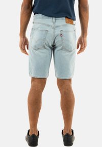 Bermudas de mezclilla azul claro con corte recto, que cuentan con dos bolsillos traseros y un parche de cuero en la cintura. Llevadas con zapatos negros.