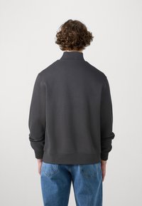 Pullover grigio scuro a maniche lunghe con collo alto, polsini e orlo a coste; mostrato di spalle. Vestibilità casual, texture del tessuto liscia.