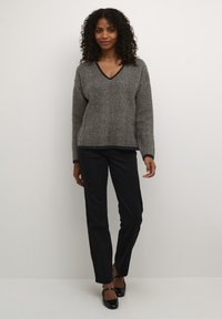 Pulover tricotat cu model herringbone în nuanțe de gri și negru, cu decolteu în V și mâneci lungi, asortat cu pantaloni negri tapered și pantofi negri. Textură netedă.