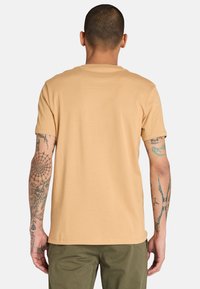 T-shirt a maniche corte con collo rotondo in cotone beige chiaro, caratterizzato da una texture liscia. Il retro non presenta motivi o loghi distintivi.