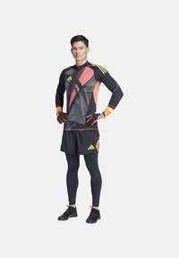 Maglietta sportiva nera con motivi geometrici multicolori, maniche lunghe, abbinata a pantaloni shorts neri e leggings, con logo del marchio e guanti.