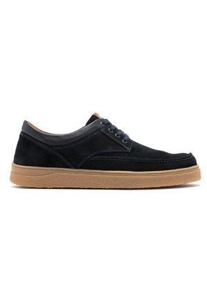 Zapatos informales de ante negro con suela de goma en tono miel, punta redonda y acentos en azul marino. Presentan un diseño de cordones y sutiles detalles de costura.