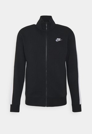 Schwarze Nike Jacke mit Reißverschluss, weißen Streifen an den Ärmeln und weißem Nike-Logo auf der linken Brust, mit hohem Kragen und gerippten Bündchen.