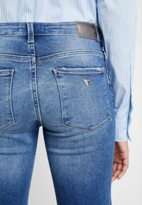 Tynde blå denimjeans har en høj talje, subtil slidtage og baglommer med en mærket trekantet metalaccent.