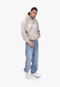 Hellgraue Kapuzenjacke mit weißem "Dropsia"-Text, kombiniert mit hellblauen Jeans und weißen Sneakern. Verfügt über eine vordere Tasche und einen entspannten Schnitt.