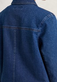 Džínová bunda z tmavě modré látky, s viditelným šitím a klasickým límcem. Obsahuje design zadního sedla a jemnou texturu.