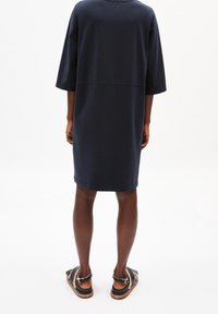 Granatowa sukienka bawełniana o luźnym kroju, z rękawami 3/4 i okrągłym dekoltem. Noszona z czarnymi sandałami z paskiem i klamrą.