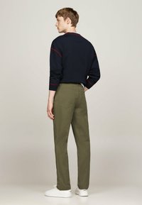 Felpa blu marina con cuciture di accento rosso, pantaloni verdi e sneakers bianche. L'outfit presenta una vestibilità rilassata e un design semplice.