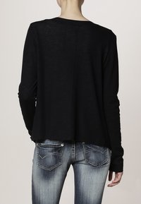 Svart långärmad topp med avslappnad passform, med rundad halsringning, rak skärning och råkant i fållen. Matchas med blå denimjeans.